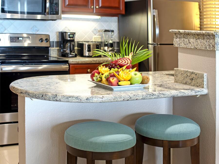 A kitchen with a granite countertop, stainless steel appliances, and a fruit display.