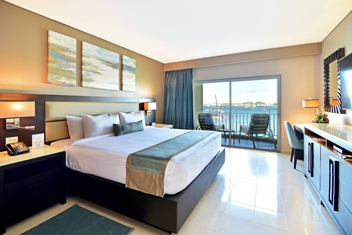A modern hotel room with a large bed, a desk, a chair, and a balcony with a view.