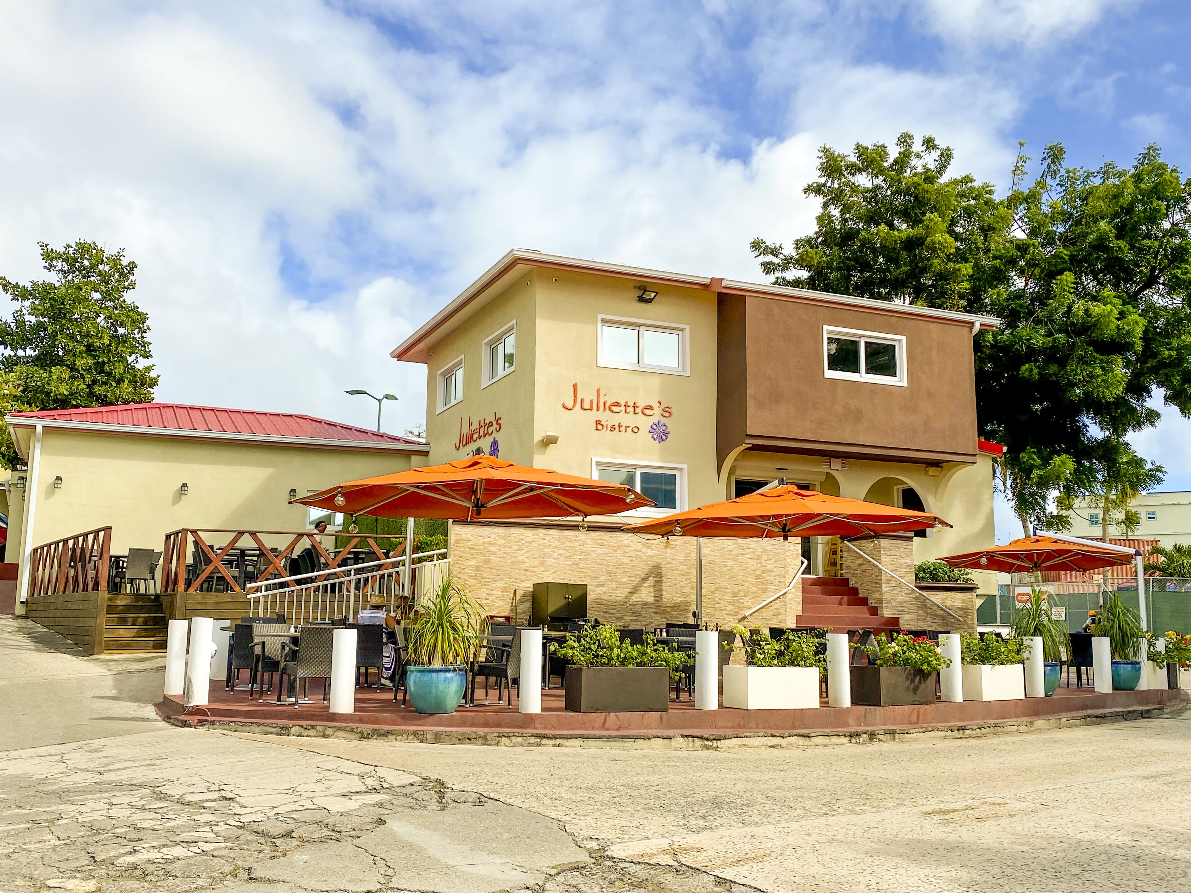 A two-story building with a sign reading "Juliette's Bistro". There are outdoor tables and chairs with orange umbrellas, and potted plants around the seating area.