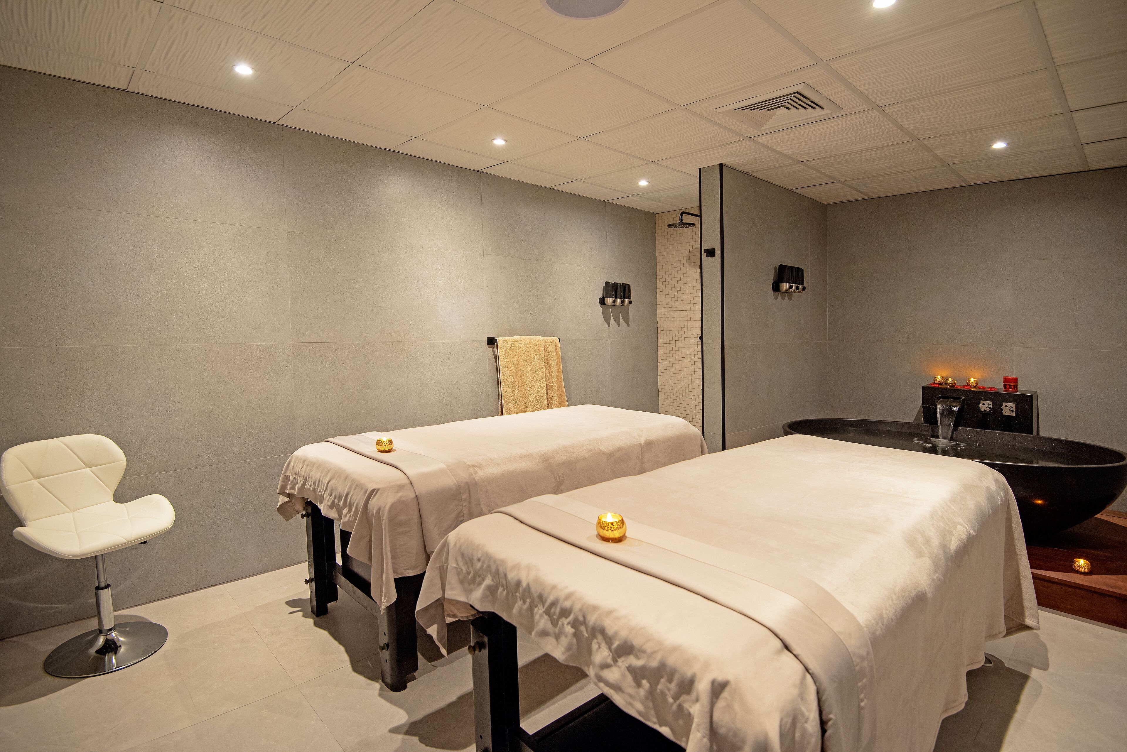 A spa room with two beds, a massage chair, and a large black bathtub.