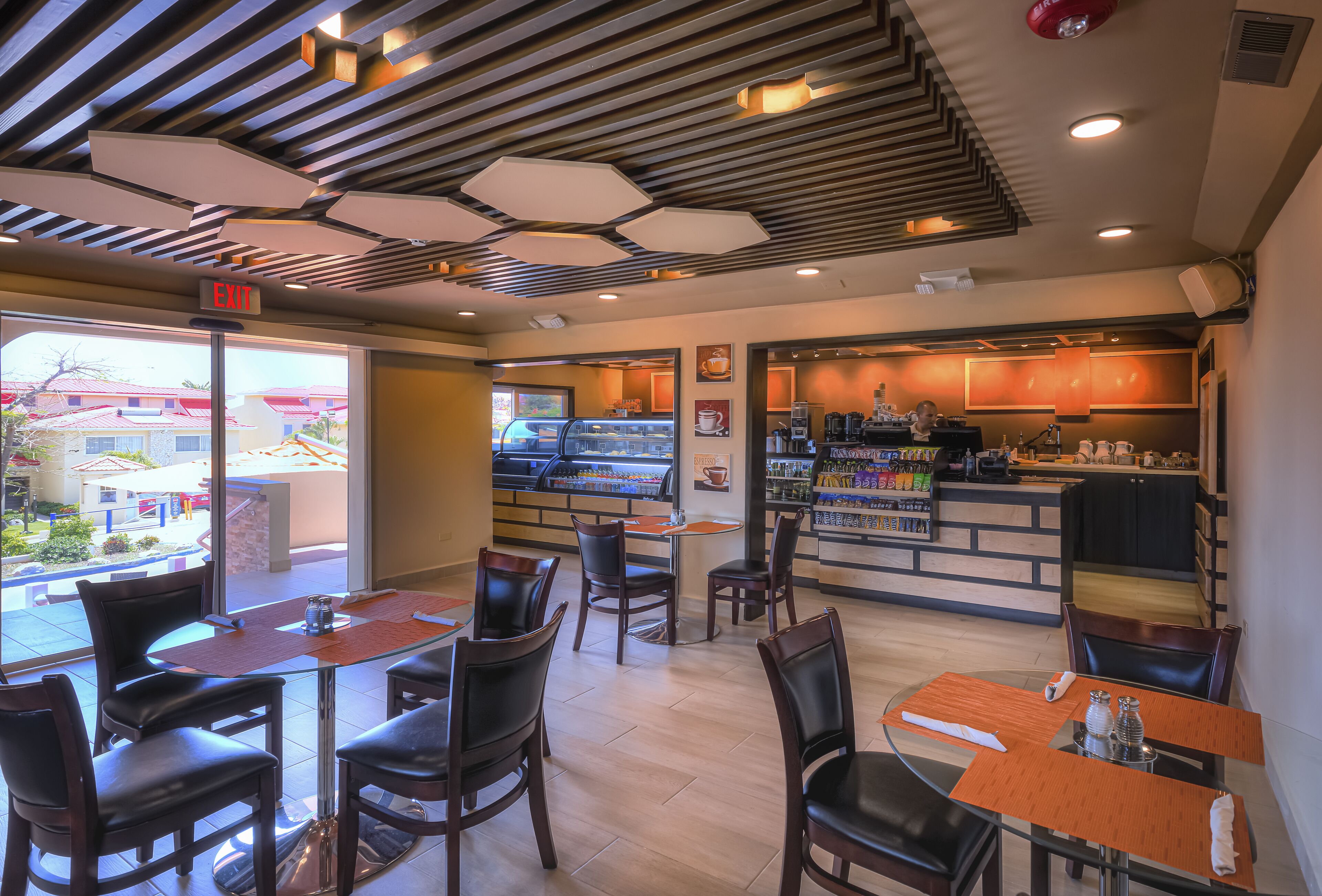 A cafe with tables and chairs, a counter with a coffee machine, and a view of the outside.