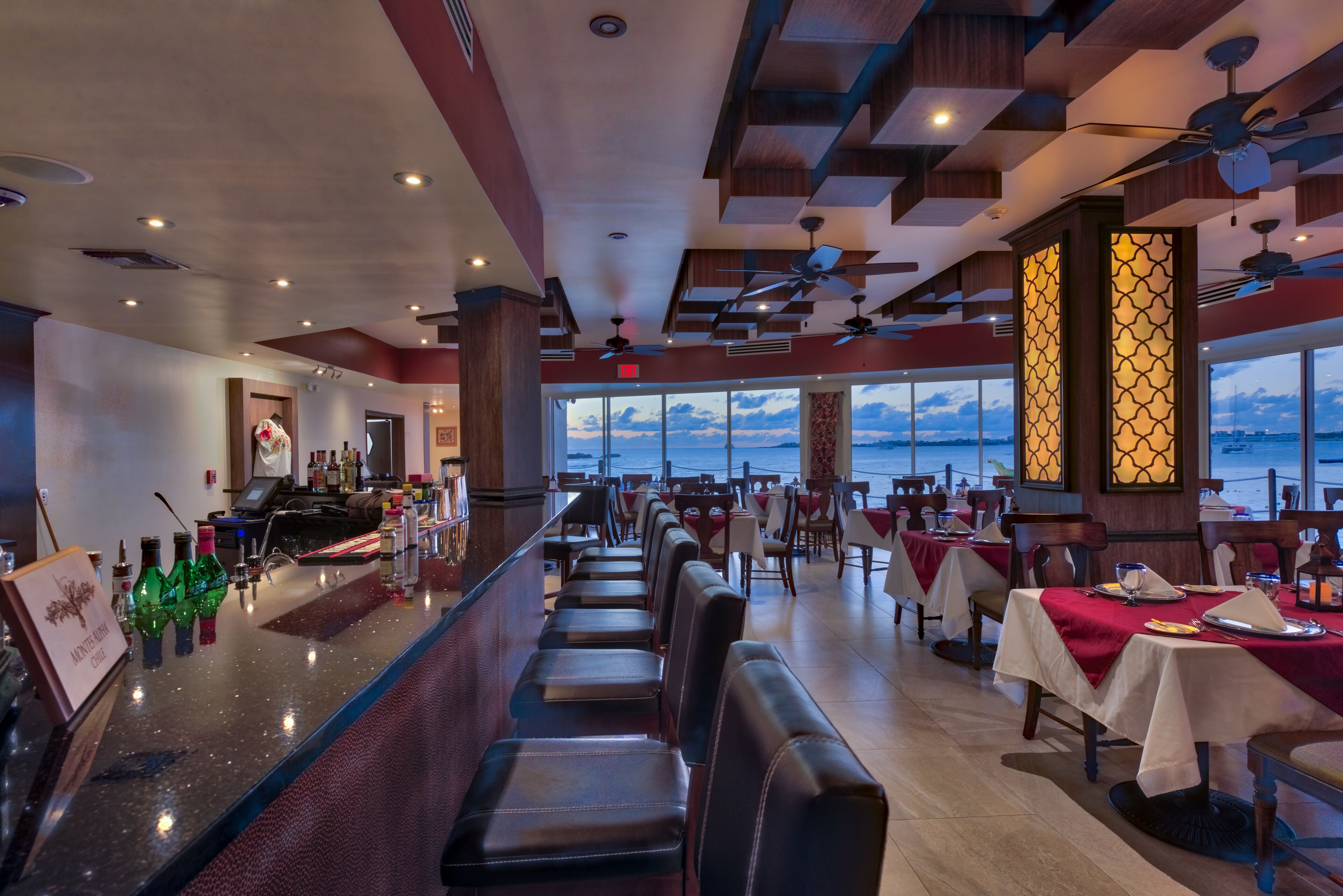 A restaurant with a bar area, seating, and a view of the ocean.