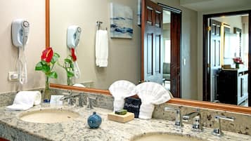 A hotel bathroom with two sinks, a mirror, a hairdryer, a vase with flowers, and a towel rack.