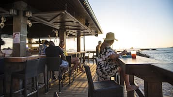 Um restaurante à beira-mar com mesas ao ar livre, área coberta e vista para o oceano.
