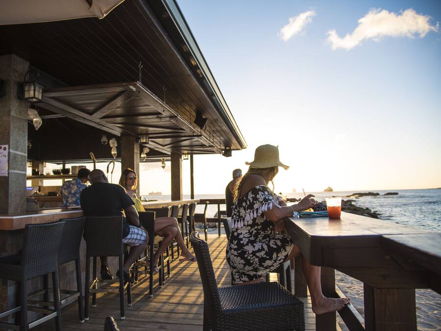 Um restaurante à beira-mar com mesas ao ar livre, área coberta e vista para o oceano.