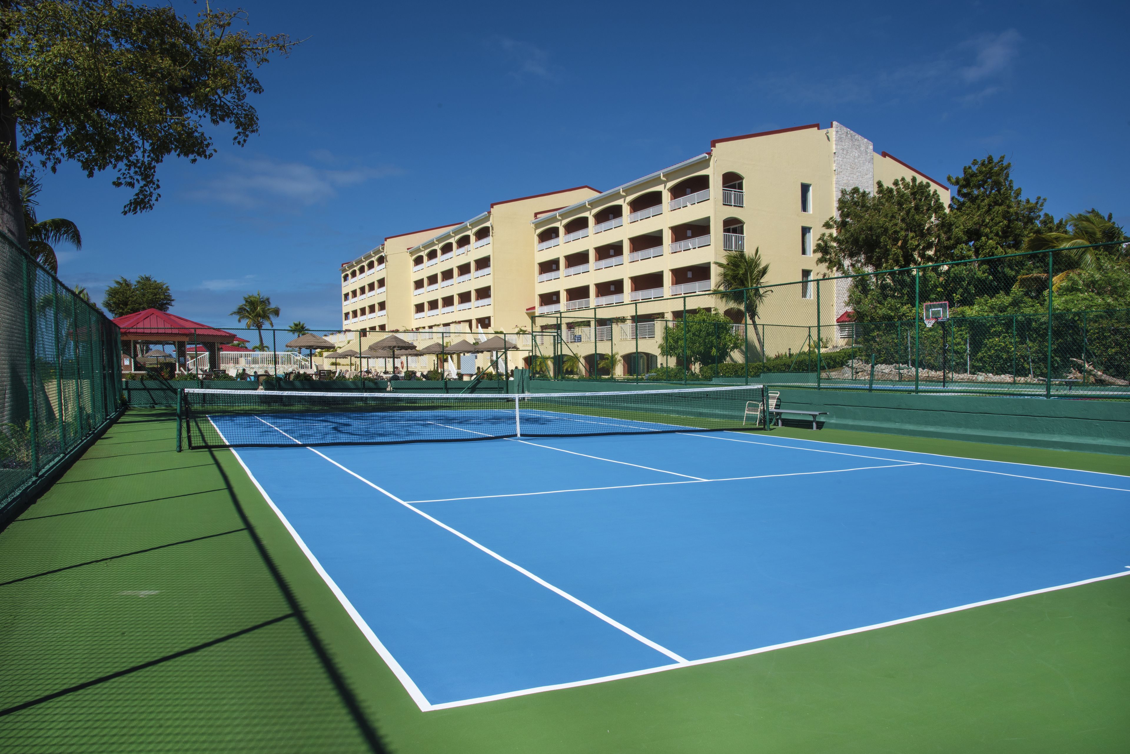 Hotellin vieressä sijaitsee ulkotenniskenttä. Hotellissa on useita parvekkeita ja sen rakennuksen katto on punainen.