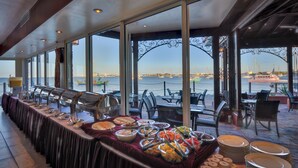 Montaje de bufé con diversas opciones de comida y vista al puerto deportivo a través de grandes ventanales.