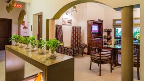 A lobby with a reception desk, a fire exit sign, a television, and a seating area with patterned chairs. - Home@F37 (New Delhi)