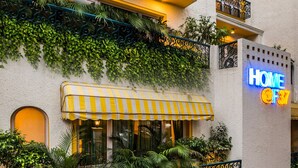 A hotel with a yellow and white striped awning, a neon sign reading "HOME OF 37", and lush green plants covering the walls. - Home@F37 (New Delhi)