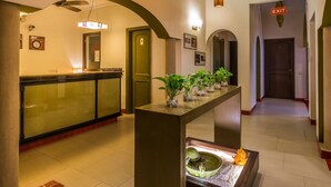 A hotel lobby with a reception desk, a waiting area with a bench, a small indoor garden, and an exit sign. - Home@F37 (New Delhi)