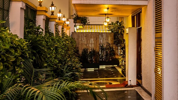 A well-lit corridor with a tiled floor, surrounded by lush green plants and decorative lighting fixtures. - Home@F37 (New Delhi)