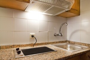 Ett kök med vita kakelväggar, en bänkskiva i granit, en diskho i rostfritt stål och en inbyggd köksfläkt.