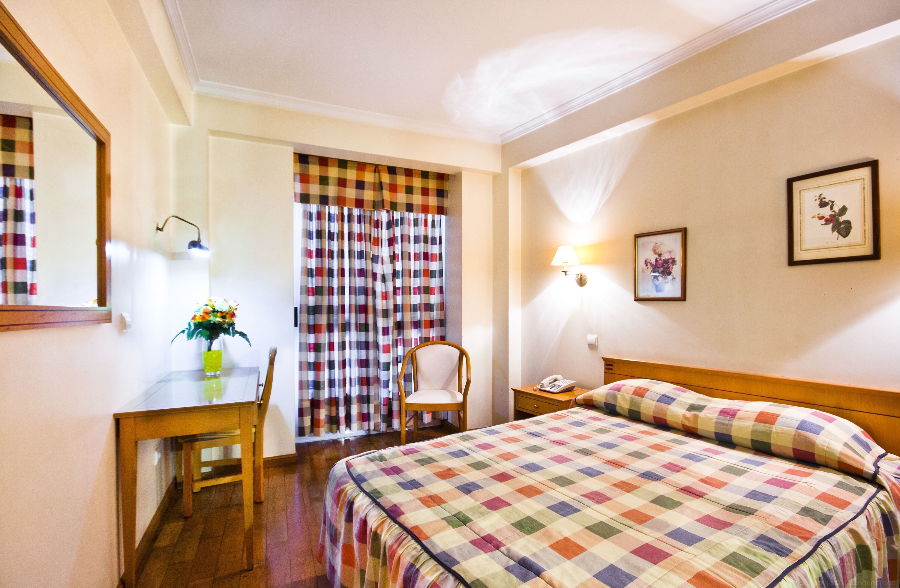 A hotel room with a bed, a desk, a chair, a nightstand, and a lamp.