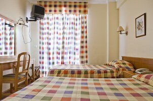 Hotellihuone, jossa on kaksi sänkyä, työpöytä, tuoli, televisio ja lamppu.