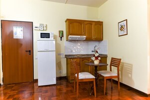 A compact kitchen with wooden cabinets, a white refrigerator, a microwave, and a small dining table with two chairs.