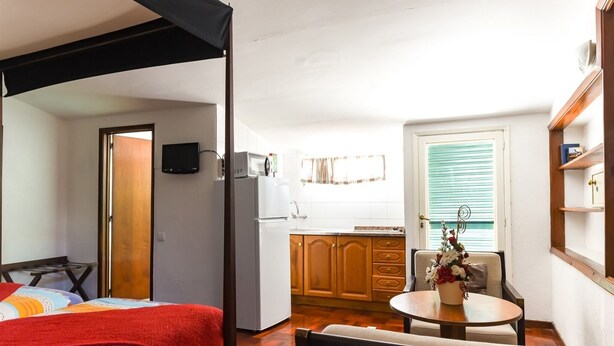 A compact room with a bed, a small kitchenette, a dining area with a table and chair, and a window with blinds. - Residencial Colombo (Funchal)