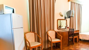 A hotel room with a wooden desk, two chairs, a mirror, a lamp, and a refrigerator. - Residencial Colombo (Funchal)