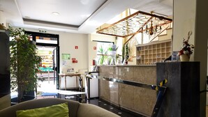 A hotel lobby with a reception desk, a seating area with a sofa, a large plant, and a staircase with a decorative railing. - Residencial Colombo (Funchal)