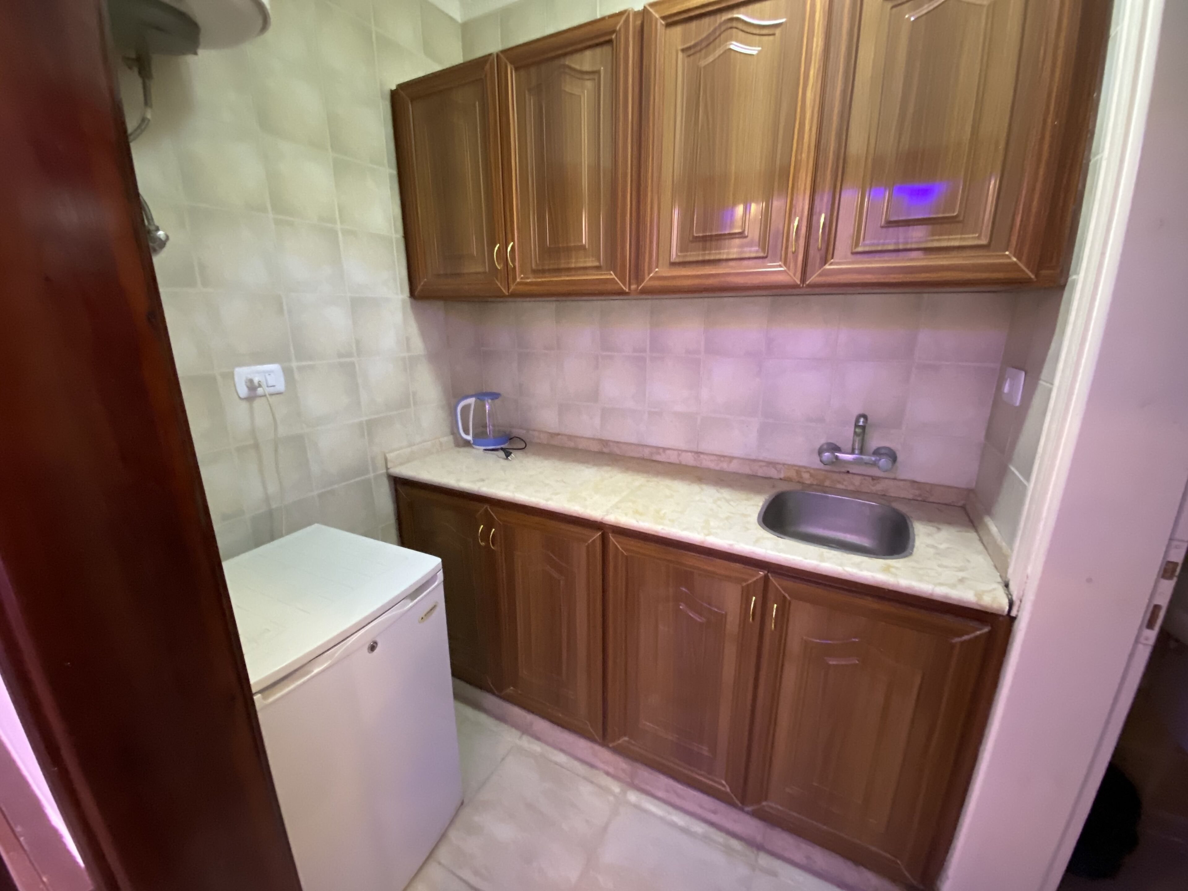 Una cucina compatta con mobili in legno, un piano di lavoro bianco, un lavandino e un piccolo elettrodomestico bianco.