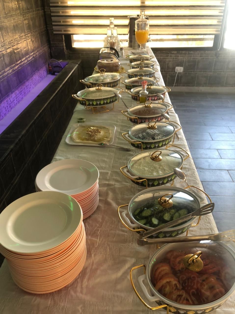 A buffet setup with various food containers and stacked plates.