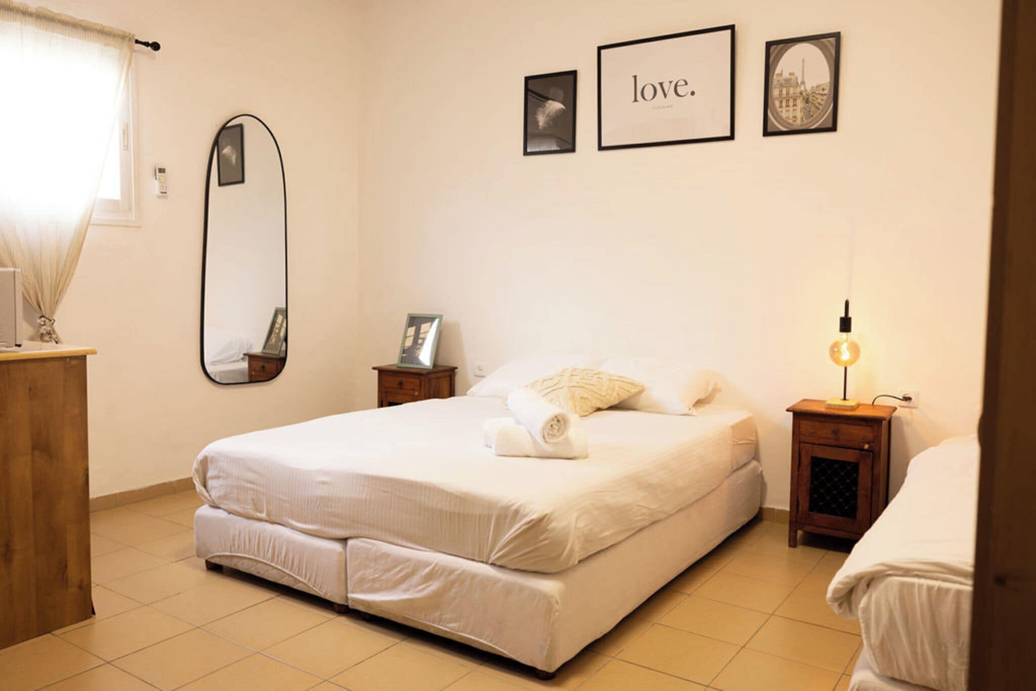 A neatly arranged bedroom with a bed, a bedside table, a lamp, and a mirror.