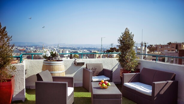 A rooftop terrace with wicker furniture, a small table with fruit, and a view of the cityscape. - Loui Talpiot Hotel (Haifa)