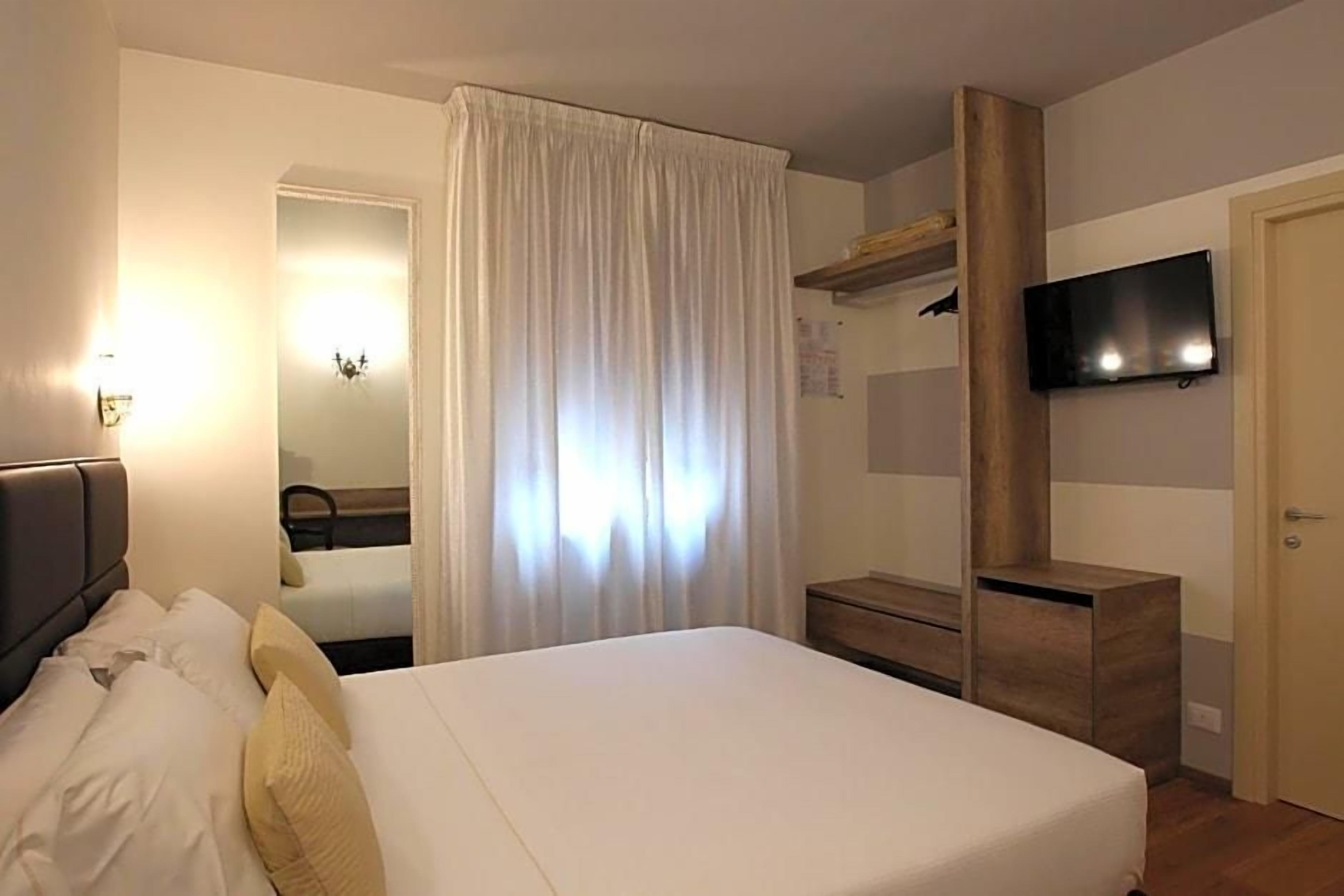 A hotel room with a bed, a television mounted on the wall, a wooden dresser, and a curtain.