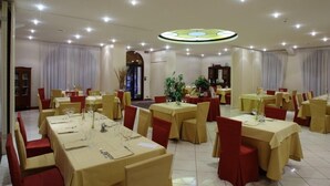 Zona pranzo con tavoli rotondi, sedie rosse e un lampadario centrale.