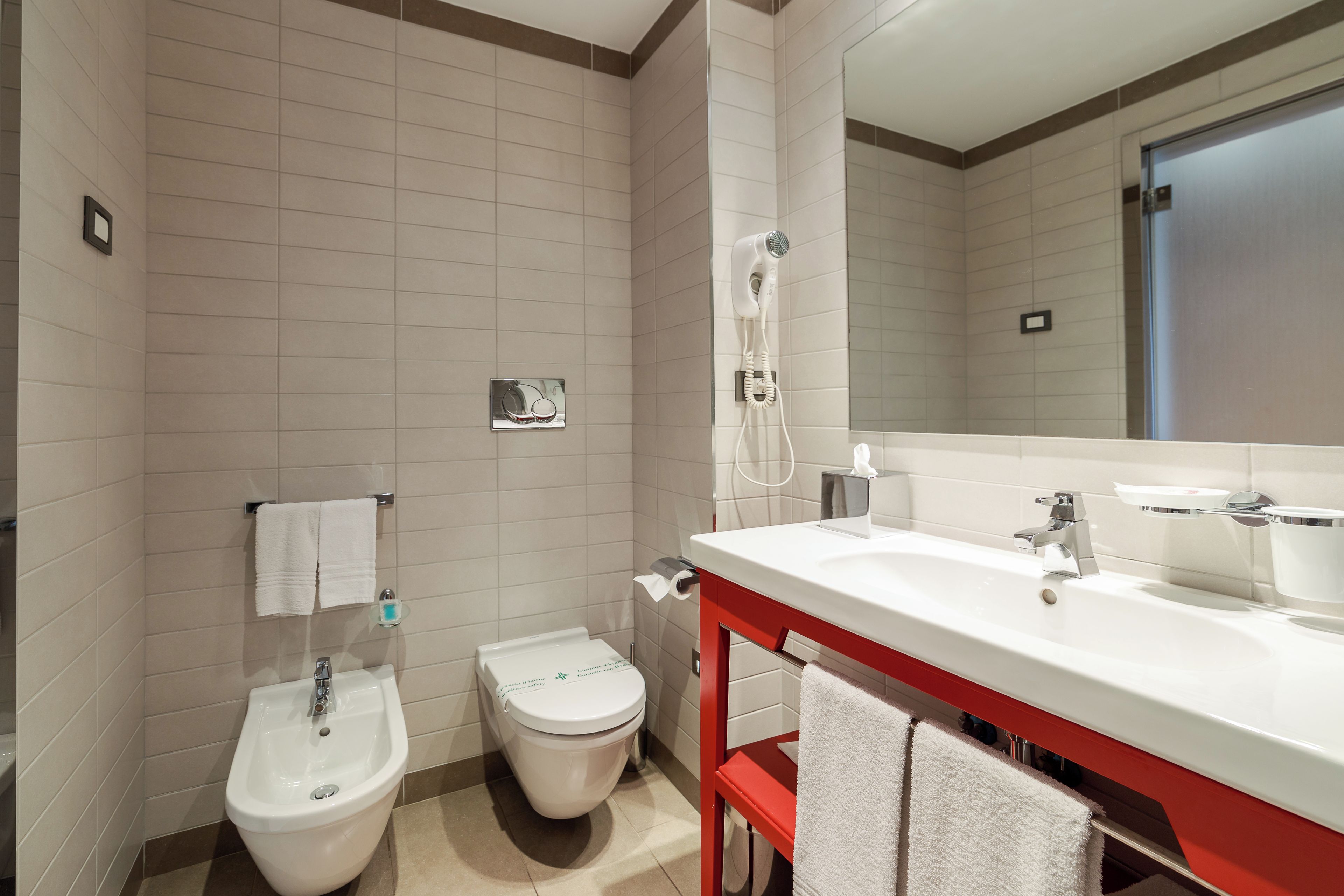 A modern bathroom with a bidet, toilet, and a large mirror above a sink.