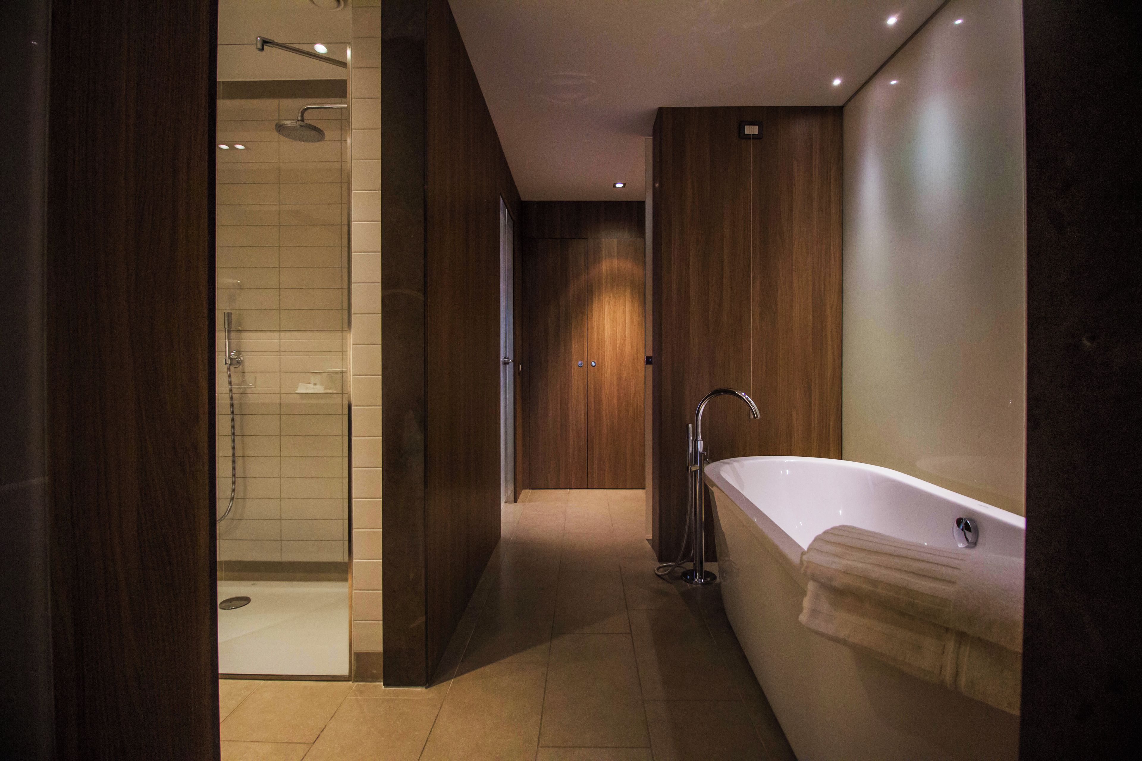 A modern bathroom with a walk-in shower, a standalone bathtub, and wooden paneling.