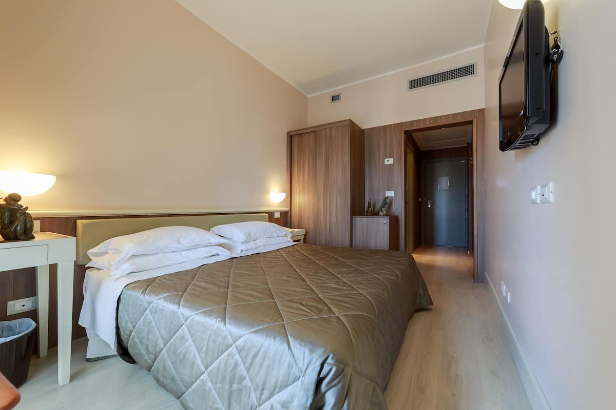 A hotel room with a bed, bedside table, lamp, wardrobe, and a television mounted on the wall.