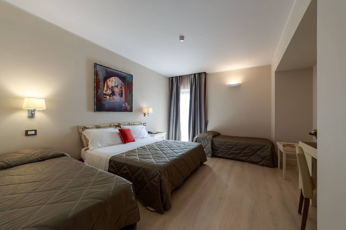 A hotel room with two beds, a desk, and a painting on the wall.