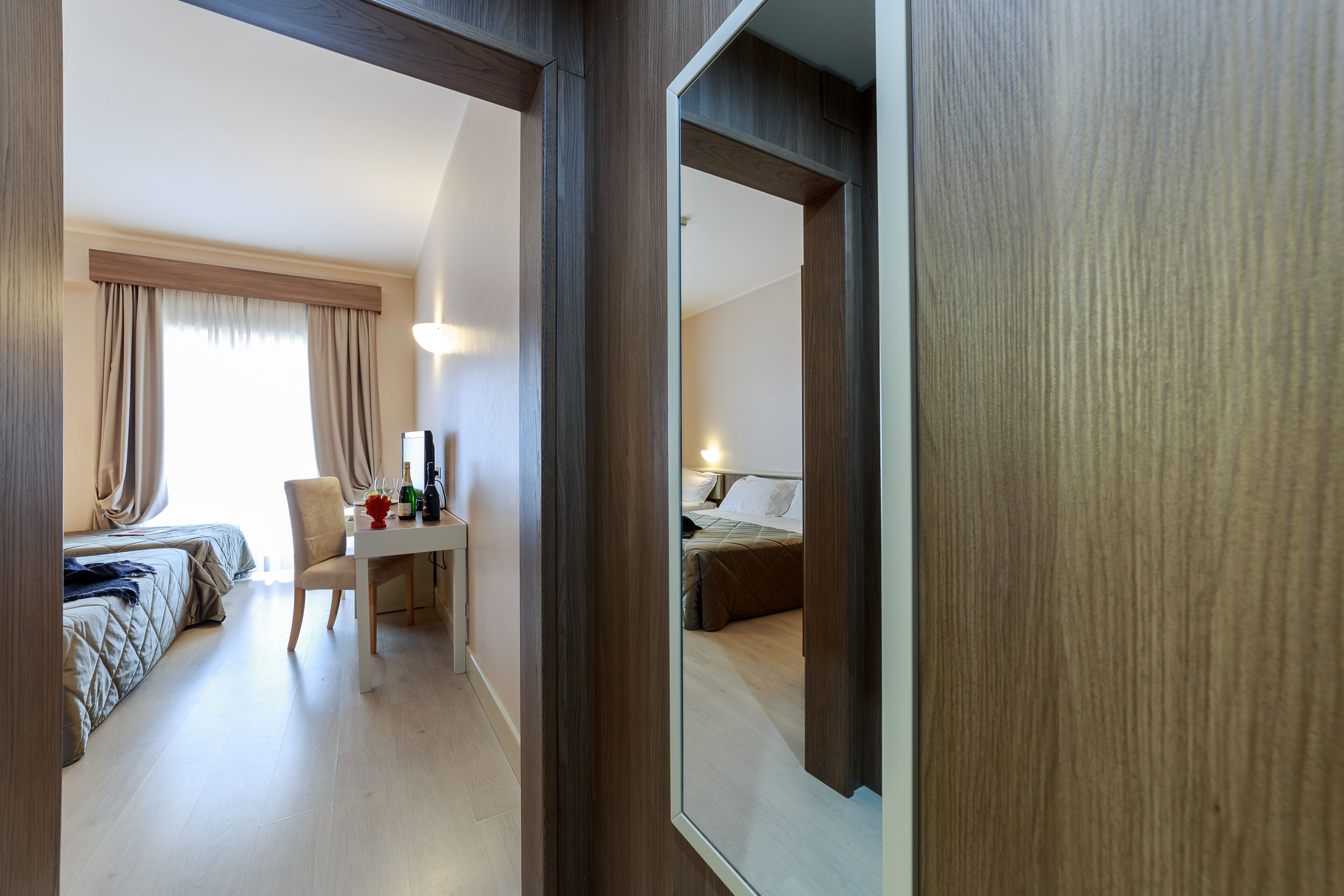 Ein Hotelzimmer mit einem Bett, einem Schreibtisch mit Stuhl, einem Spiegel und einem Fenster mit Vorhängen.