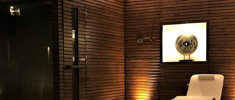 A modern bathroom with a glass shower enclosure, a white chair, and a wall-mounted light fixture.