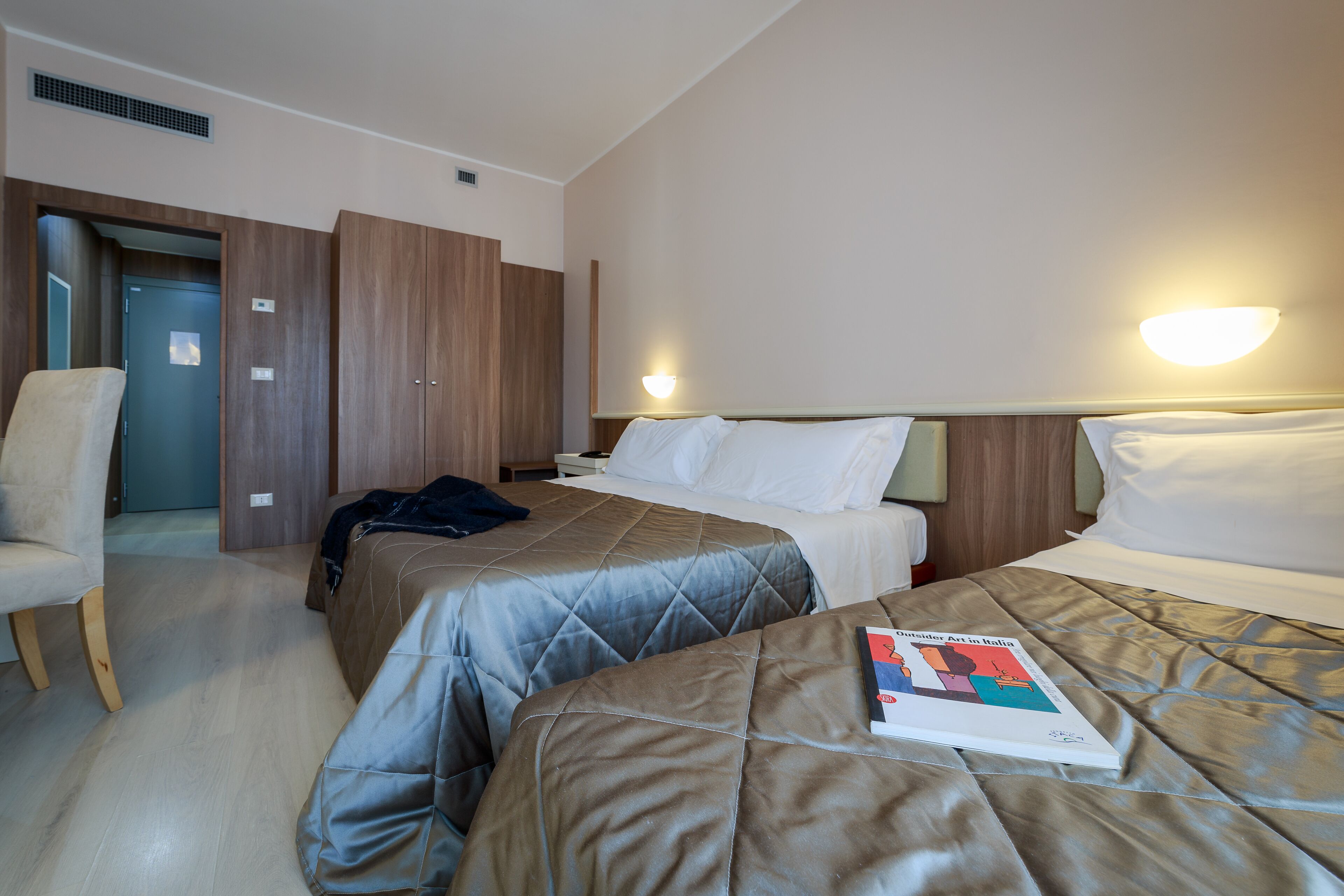 A hotel room with two beds, a chair, and a book on the bed.