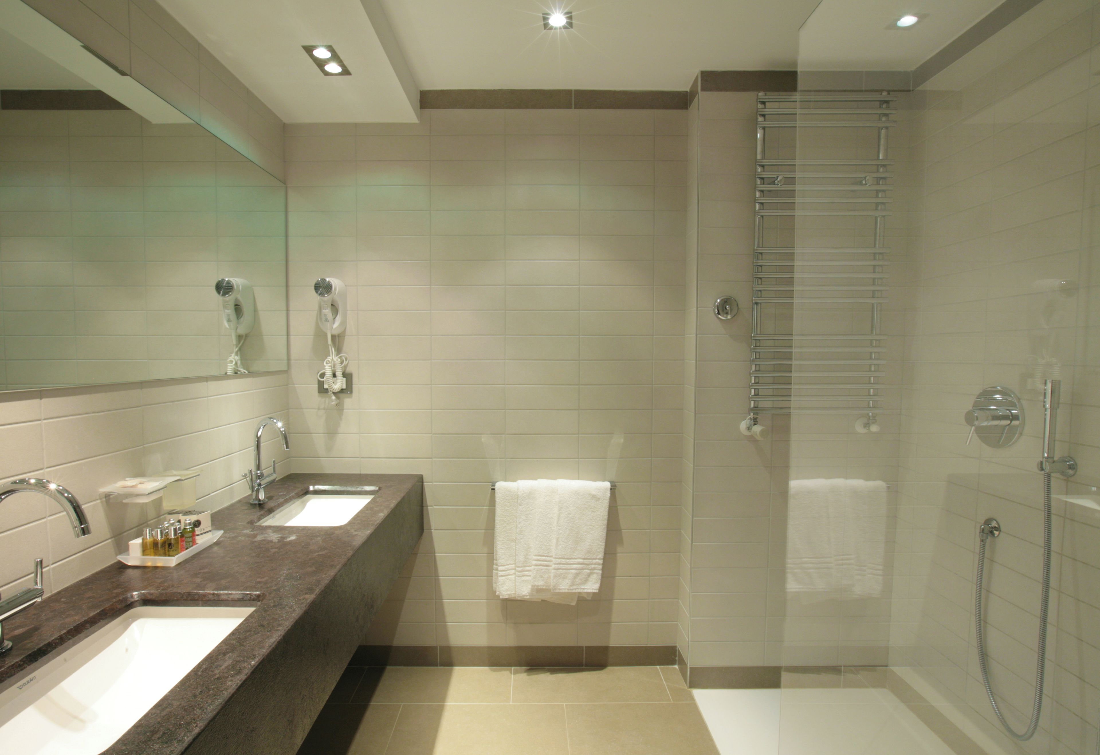 Een moderne badkamer met een wastafel met twee kommen, een grote spiegel, een douche met glazen deur en een handdoekhouder.