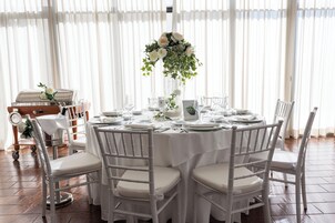 Una mesa redonda dispuesta para un evento formal, con sillas blancas y un centro de mesa floral.