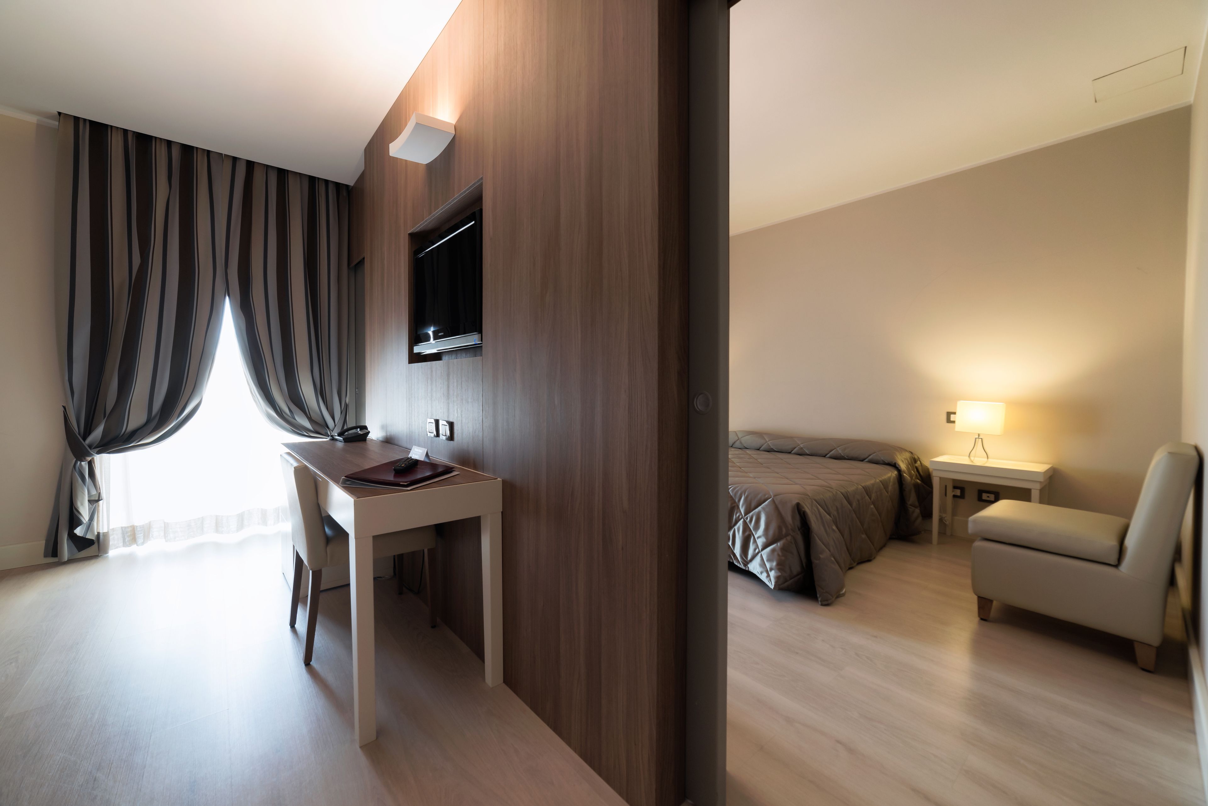 A modern hotel room with a desk, a bed, a chair, and a TV.