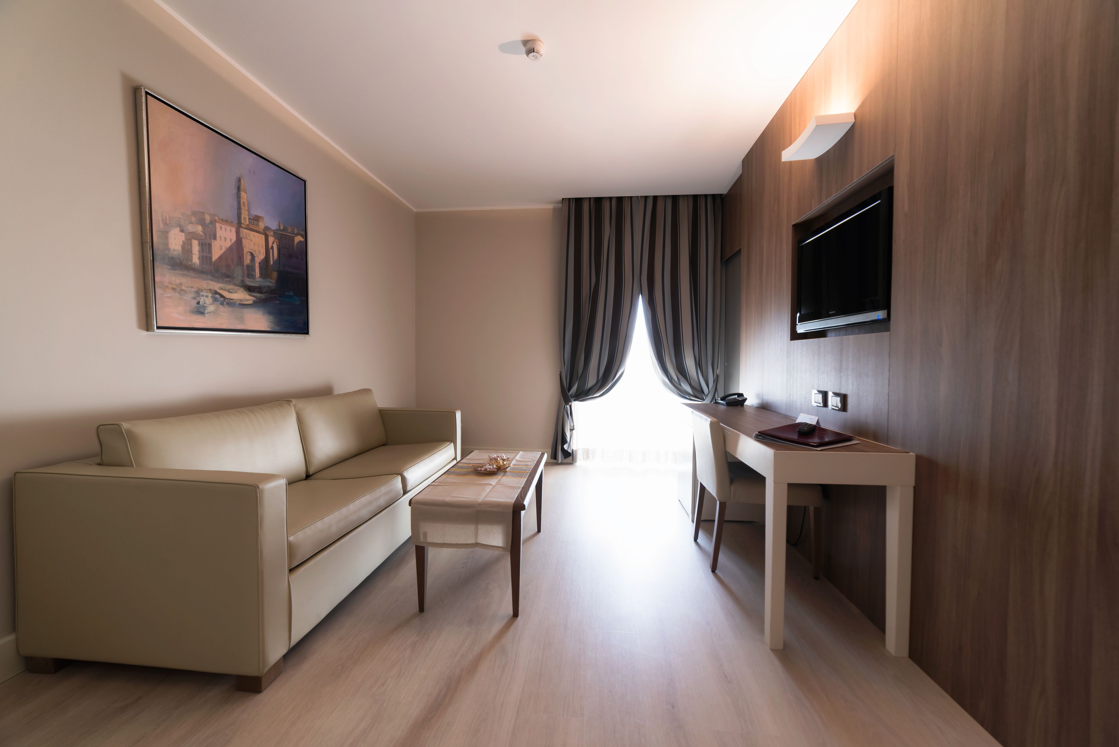 A modern living room with a sofa, a coffee table, a flat-screen TV mounted on the wall, and a painting on the wall.