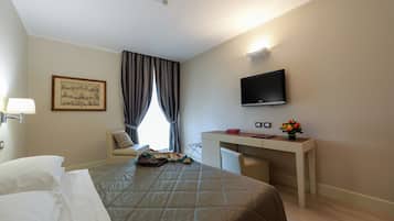 Une chambre d’hôtel comprenant un lit, un bureau, une télévision, une fenêtre avec des rideaux et un tableau accroché au mur.