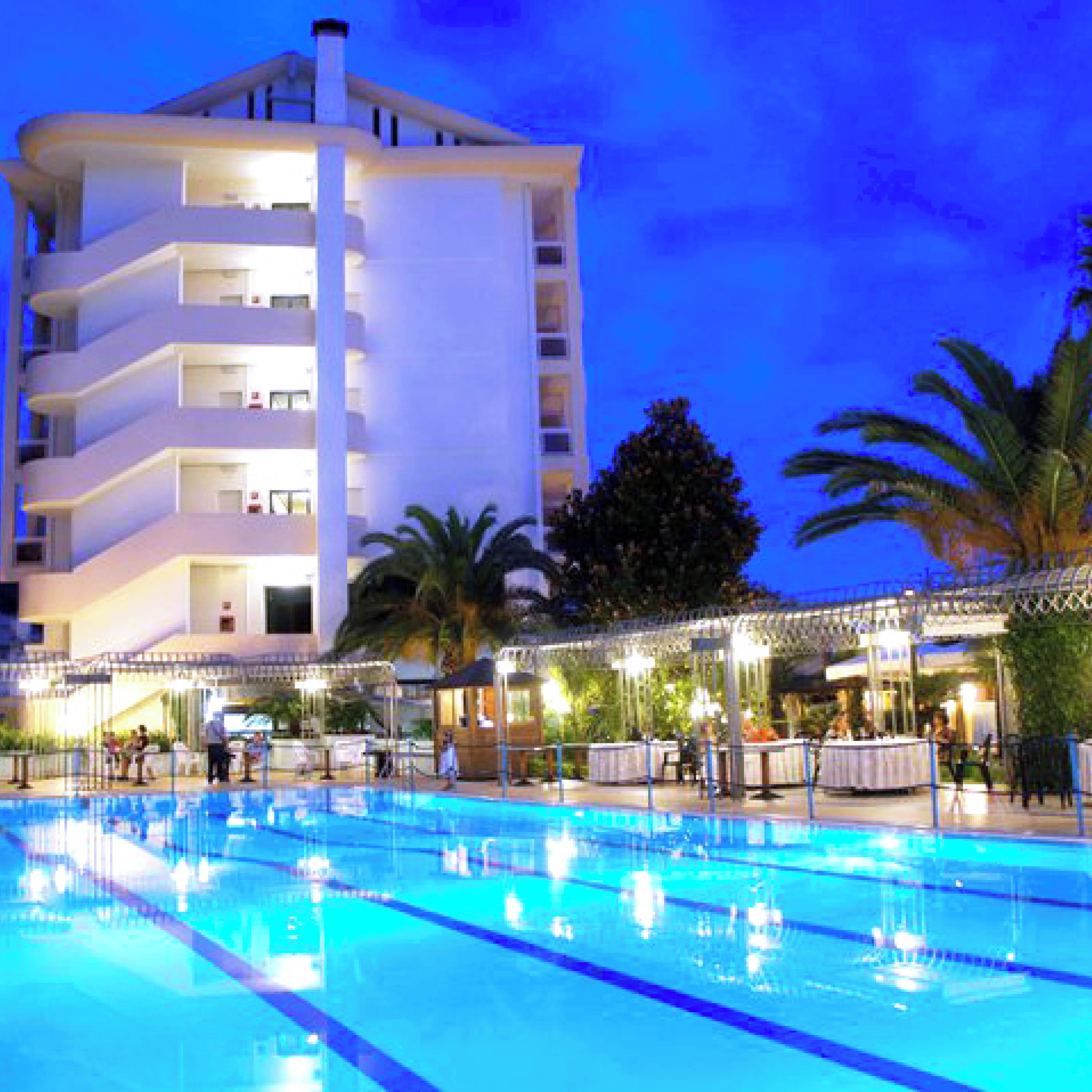A hotel with a swimming pool, outdoor seating, and a multi-story building.