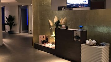 Et moderne receptionsområde med en receptionsdisk, en tv-skærm og en dekorativ plante.