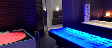 A modern spa room with a heated stone bath, a massage table, and a sauna.