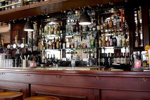 A bar with multiple shelves of liquor bottles, a bar counter, and hanging lights. - Hotel Abcoude (Abcoude)