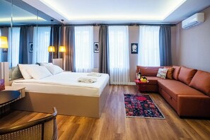 A hotel room with a bed, a sofa, a small table with a bottle and glasses, a chair, and a rug. - Cheers Porthouse (Istanbul)