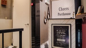 Un pasillo con piso a cuadros, una señal de salida, una puerta y un cartel que dice "Cheers Porthouse" con una lista de valores.
