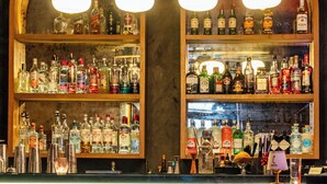 Zona de bar con estantes llenos de botellas de licores, un letrero de neón que dice 'Cheers' y un área de asientos con mesas y sillas.