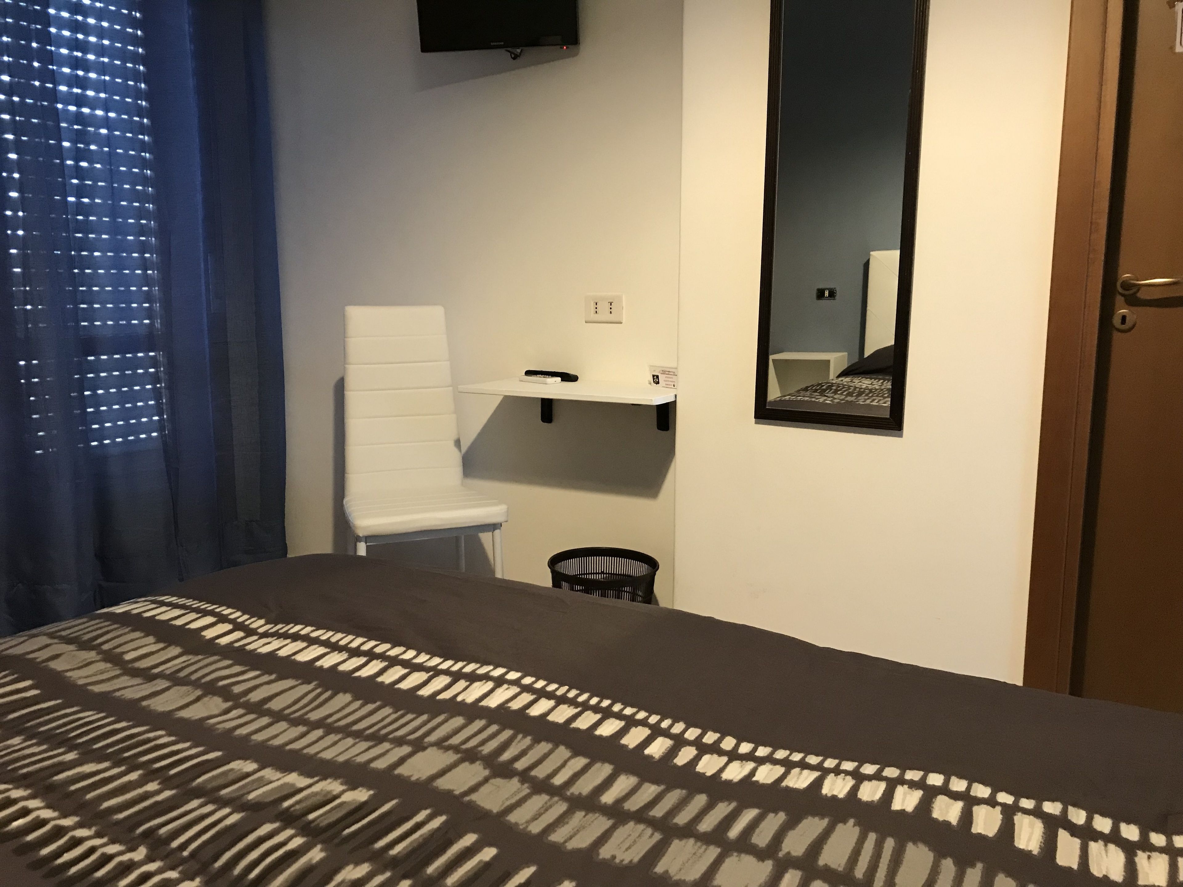Een slaapkamer met een bed, een stoel, een klein tafeltje, een spiegel en een deur.