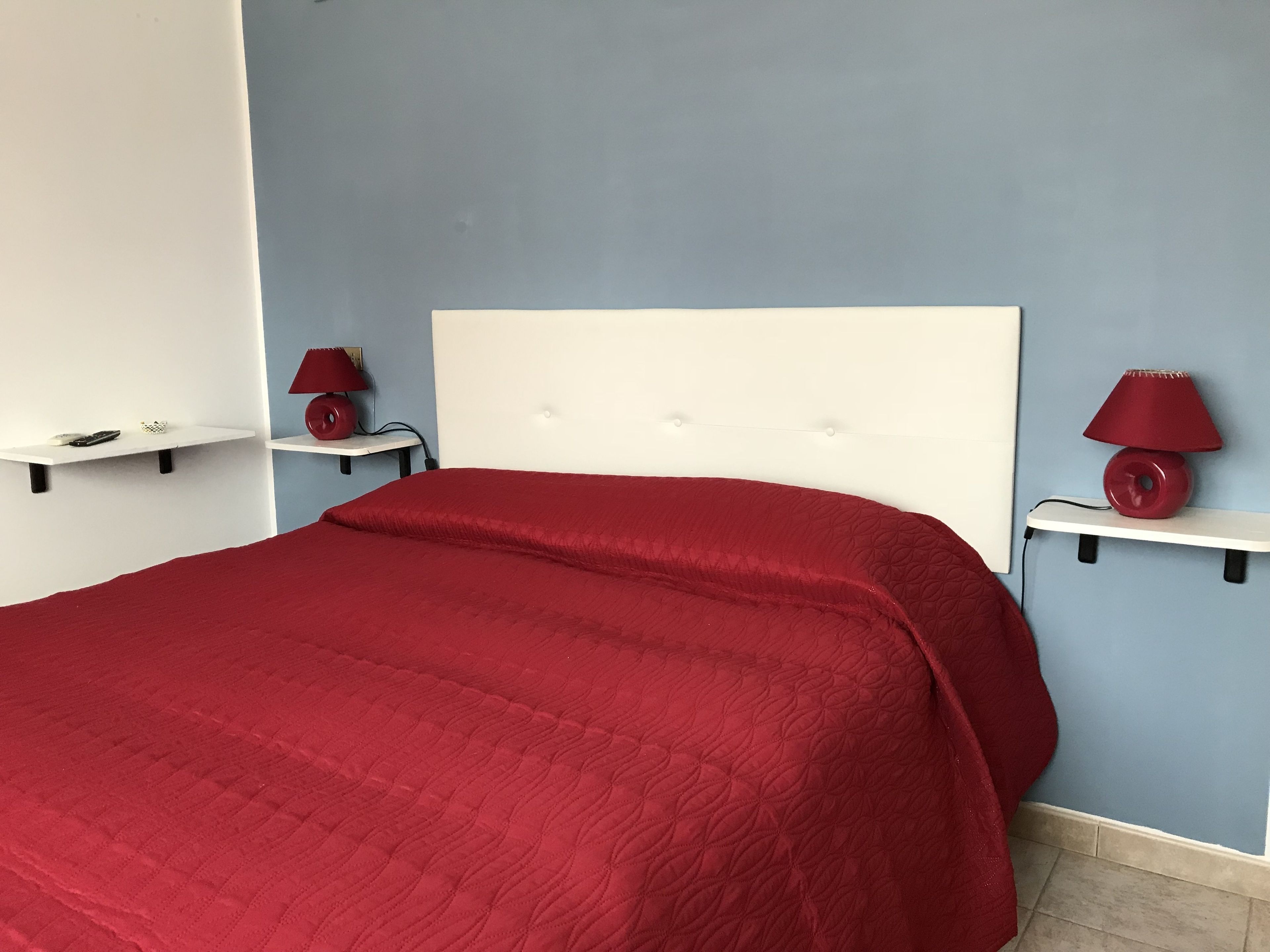 Ein Bett mit roter Bettdecke, zwei Nachttische mit Lampen und eine blaue Wand.