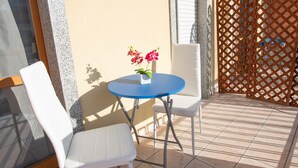 A small outdoor seating area with a round table and two white chairs, a potted plant with pink flowers, and a wooden lattice fence. - Bed and Breakfast Triscele (Sciacca)